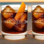 Two glasses of 'Mirage 2000'-themed cocktails with ice and an orange slice on a white background.