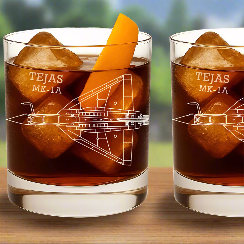 Two glasses of dark liquid with ice cubes and an orange slice, featuring 'TEJAS MK-IA' design.