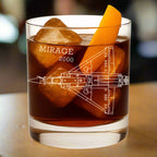 Glass of dark liquid with ice and an orange slice, featuring 'Mirage 2000' design.