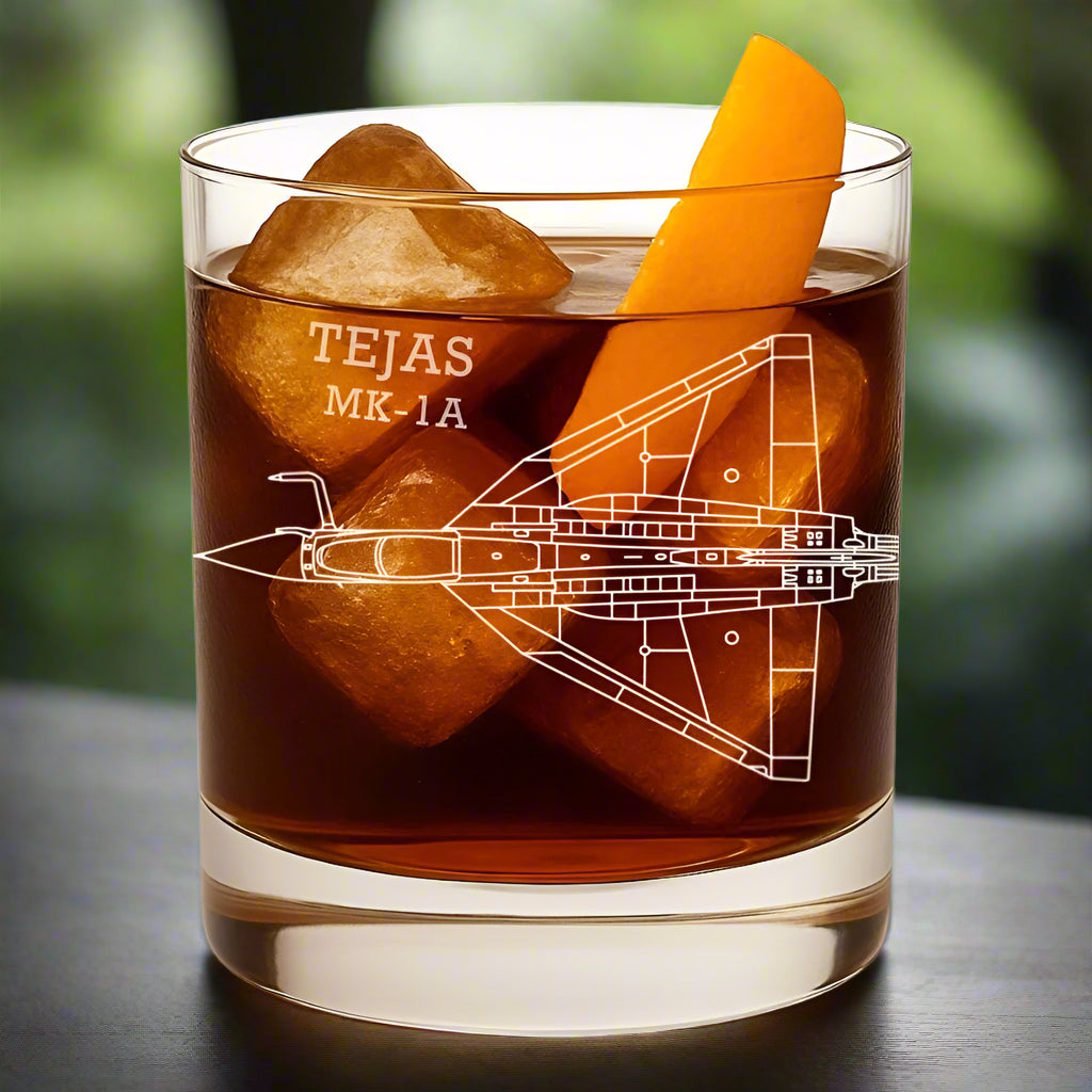Glass with a design of an airplane and 'TEJAS MK-1A' text, filled with whiskey and orange peel.