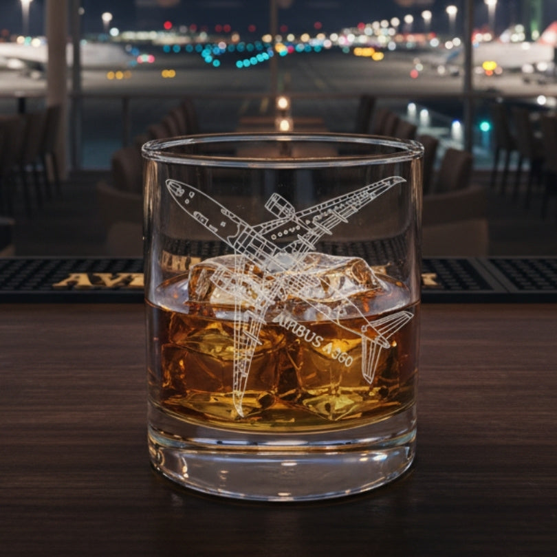 Glass of whiskey with ice and an airbus A350 airplane engraving on a bar counter at an airport at night.