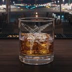 Glass of whiskey with ice and an airbus A350 airplane engraving on a bar counter at an airport at night.