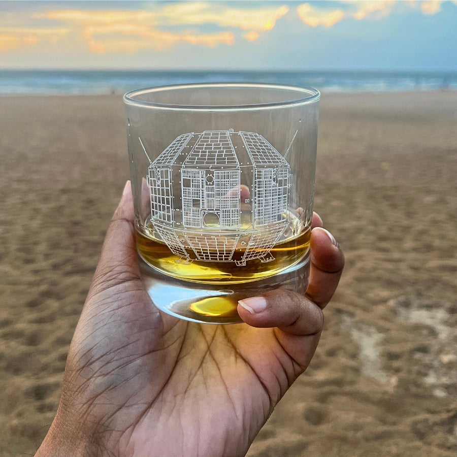 An whiskey glass engraved with the first indian satellite called aryabhata at a seaside beach in Goa.