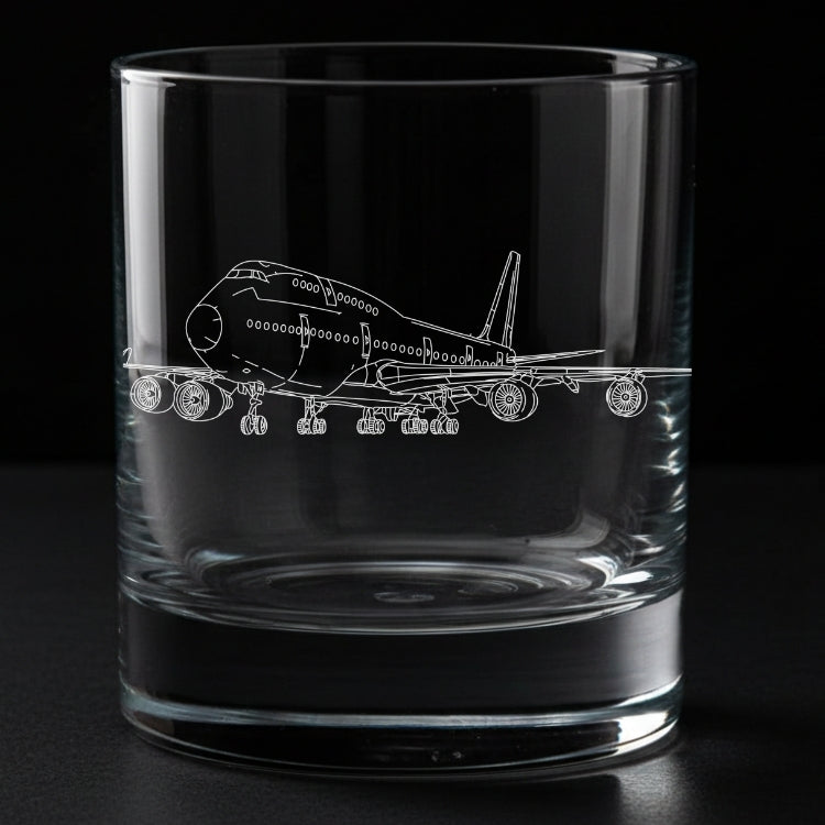 A clear glass rocks tumbler with an etched outline of a boeing 747 passenger airplane on the front, shown against a solid black background.