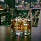 Glass of whiskey with ice cubes and a boeing 747 airplane engraving on a bar counter.