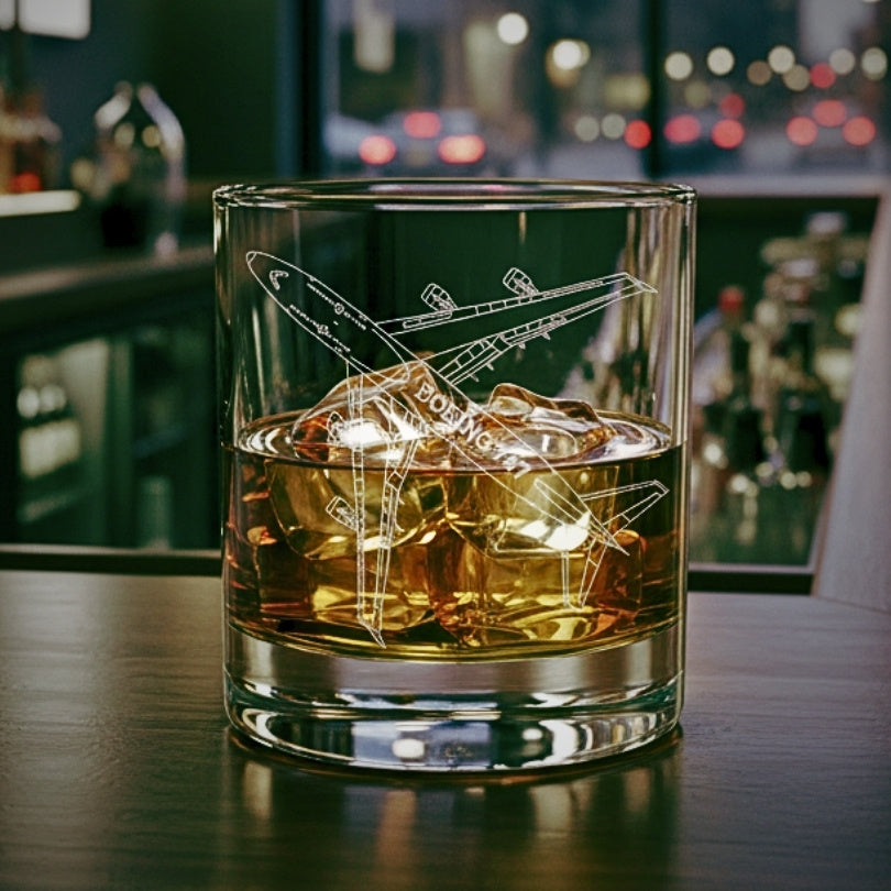 Glass of whiskey with ice cubes and a boeing 747 airplane engraving on a bar counter.