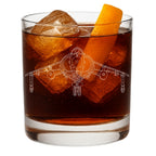 A clear rocks glass filled with an amber-brown cocktail, large ice cubes, and an orange peel garnish, shown on a white background. The glass is etched with a detailed white line drawing of a hawker harrier fighter jet.