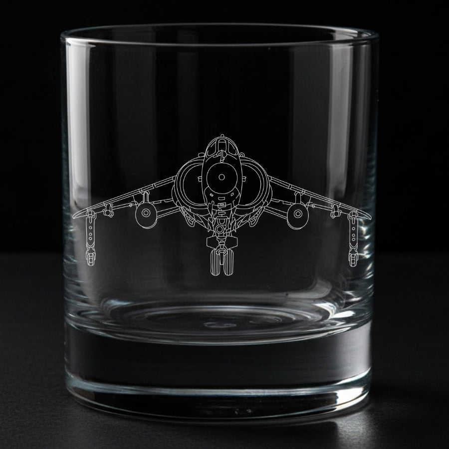A clear glass rocks tumbler with an engraved line drawing of a hawker Harrier fighter jet on the front, set against a solid black background.