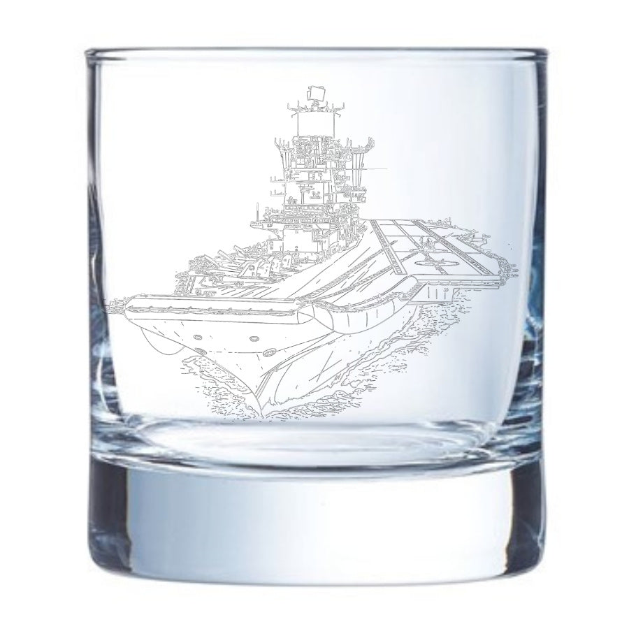 Clear glass tumbler with an engraved aircraft carrier ship INS Vikramaditya design on a white background