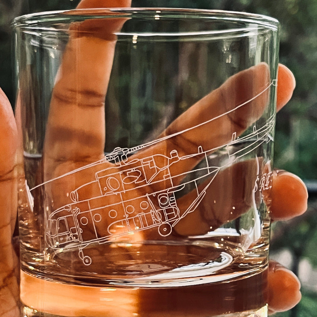 Clear glass with mi-17 helicopter engraving held in a hand against a blurred green background