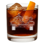 Glass of dark liquid with ice and an orange peel, featuring a t71 tank blueprint etching.